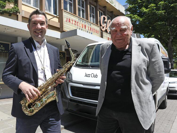 Zwei Funktionsträger des Jazz Clubs stehen vor dem Eingang des Konzertsaals. Ein Mann hält ein Saxofon in der Hand.